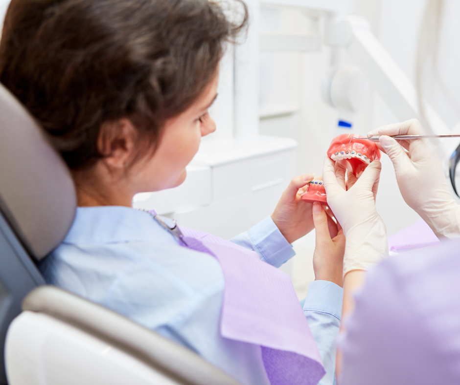An orthodontist shows a patient a model of teeth with braces during an in-person exam