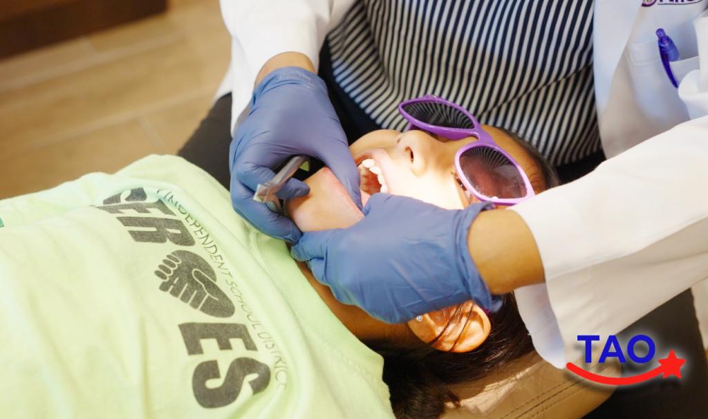 Una joven paciente acostada en una silla de ortodoncia mientras una ortodoncista de Texas le examina los dientes.