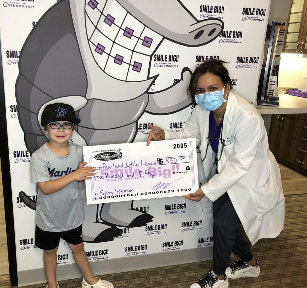 Dr. Sheela Kudchadker of Pearland Orthodontics and a little boy hold a check made out to Pearland Little League