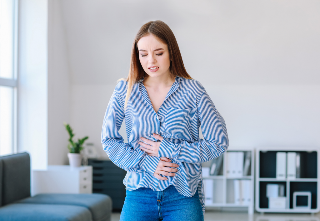 A young woman in an office holds her arms across her stomach in pain