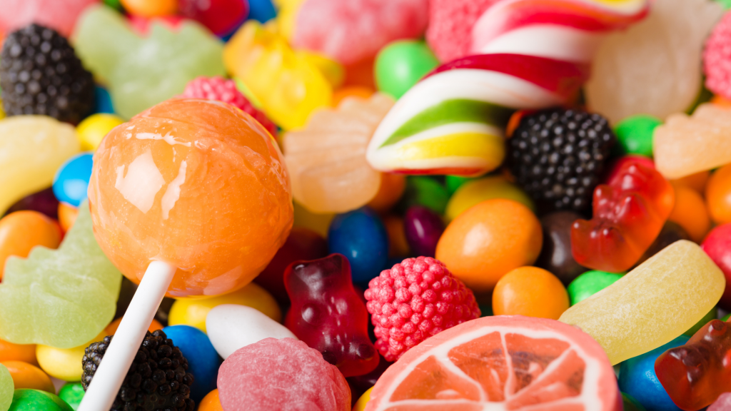 A close up of a pile of different kinds of fruity candy, such as lollipops, gummy bears, and hard candies.