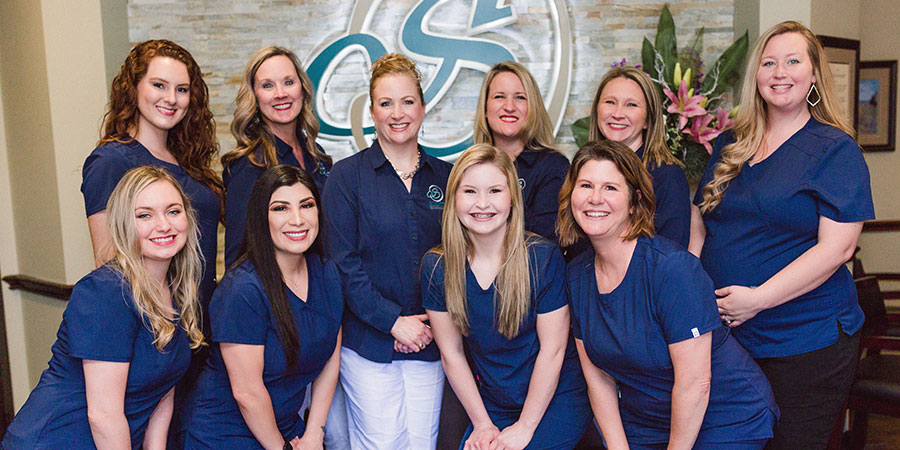 Orthodontist Dr. Meredith Scott surrounded by her smiling office staff.