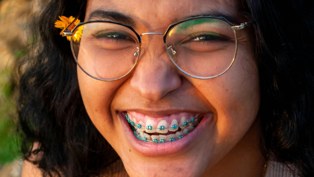 A smiling young woman with glasses, braces, and dark hair.