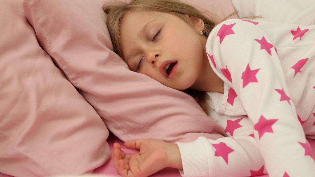 Una niña con la cabeza en la almohada duerme con la boca abierta