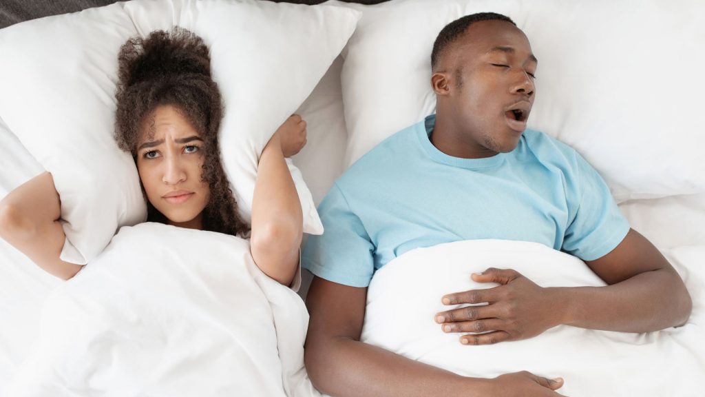 Una mujer acostada junto a su pareja que ronca se tapa los oídos con una almohada